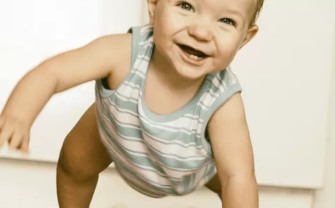 A baby smiling while learning how to walk.