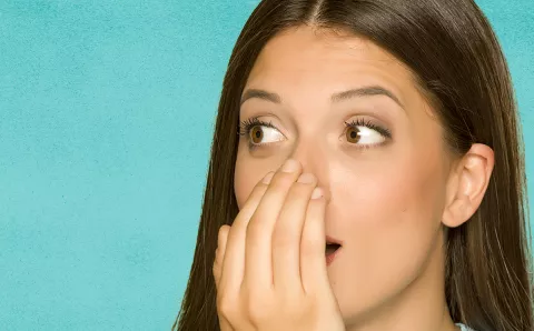 A woman exhaling into her hand to smell her breath.