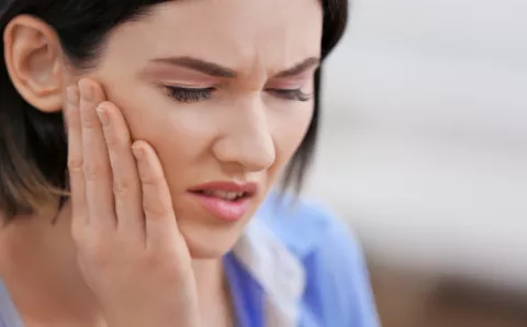 A woman with sensitive teeth feeling her jaw due to pain.