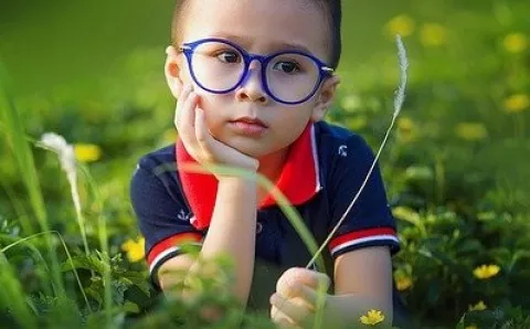 A child wearing glasses while laying in a field.