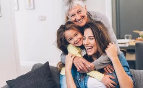 A grandmother, mother and daughter smiling in the family room.