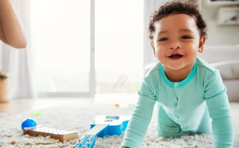 A baby with no teeth crawling on the floor.