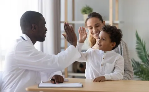 An African American dentist high-fiving his African American toddler patient who is happy after a successful dental exam.